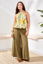Load image into Gallery viewer, Woman wearing a sleeveless multi-color top, olive green pants, brown sandals and jewelry in a bright room with a plant.
