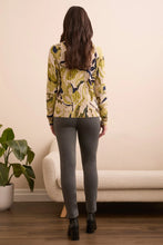 Load image into Gallery viewer, Woman wearing a floral sweater, black boots and gray pants standing in a room with a plant and sofa.
