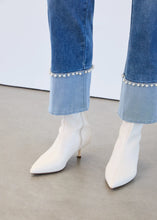 Load image into Gallery viewer, Close-up of blue jeans with pearl embellished cuffs and white boots against white wall.
