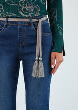 Load image into Gallery viewer, Close-up of model wearing green top and silver tassel belted blue jeans against a neutral background.

