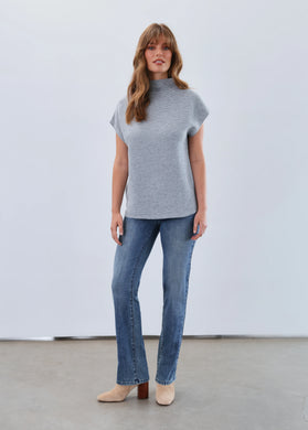 Woman wearing a light blue short sleeve sweater, blue jeans and beige boots against a white background.