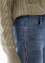 Load image into Gallery viewer, This Indigo Wash Jean with Multicolor Embroidery is the perfect addition to elevate your denim look. It features a pull-on style, faux-fly stitching, 5-pocket styling, belt loops, and a slim leg taper that can be unrolled for full length. Zig zag embroidery decorates the outer seams. Color- Indigo wash. Zig Zag embroidery colors- light blue, light orange, dark red. Pull-on style. Faux fly stitching. Five functional pockets. Zig Zag embroidery down each side. Belt loops.

