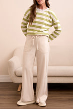 Load image into Gallery viewer, Woman wearing a green and white striped sweater, moonstone pants and sneakers in a living room setting.
