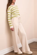 Load image into Gallery viewer, Woman wearing a green and white striped sweater, moonstone pants and sneakers against a white wall.
