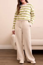 Load image into Gallery viewer, Woman wearing a green and white striped sweater, moonstone pants and sneakers in a living room setting.
