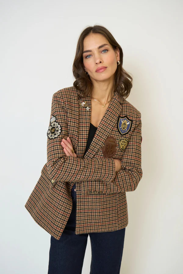 Woman wearing a plaid blazer with patches and blue jeans against a white background.