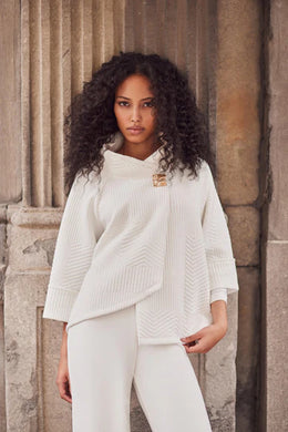Woman wearing white swing jacket and white pants standing against a stone wall.