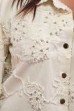 Load image into Gallery viewer, Close-up of the applique and rhinestone embroidery on a cream shacket. 

