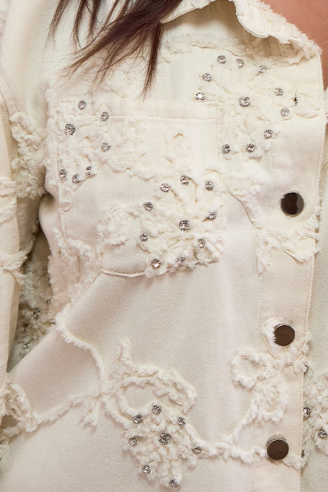 Close-up of the applique and rhinestone embroidery on a cream shacket. 