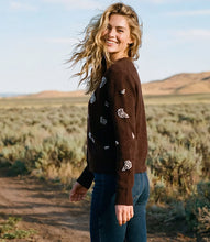 Load image into Gallery viewer, A woman stands outdoors in a desert landscape wearing a dark brown knit cardigan with rhinestone floral embroidery and blue jeans.
