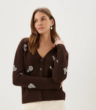 Load image into Gallery viewer, A woman wearing a dark brown knit cardigan with rhinestone floral embroidery and rhinestone drop earrings paired with cream pants, against a plain light gray studio background.
