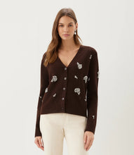 Load image into Gallery viewer, A woman wearing a dark brown knit cardigan with rhinestone floral embroidery and rhinestone drop earrings paired with cream pants, against a plain light gray studio background.
