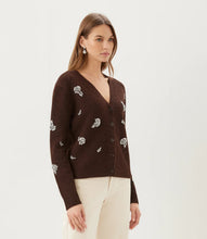 Load image into Gallery viewer, A woman wearing a dark brown knit cardigan with rhinestone floral embroidery and rhinestone drop earrings paired with cream pants, against a plain light gray studio background.
