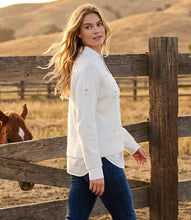 Load image into Gallery viewer, A woman stands outdoors beside a rustic wooden fence in a sunlit field, wearing a cream layer knit sweater with decorative flower appliqués and blue jeans. A horse is partially visible behind the fence.
