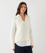Load image into Gallery viewer, A woman modeling a cream-colored layered knit sweater with 3D floral embroidery, and dark blue jeans, against a plain white studio background.
