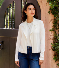 Load image into Gallery viewer, Woman wearing an off-white jacket over an off-white top and blue jeans standing in front of a door with an archway.
