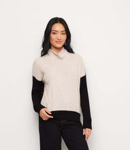 Load image into Gallery viewer, A woman modeling a colorblock turtleneck top with an oatmentl body and black sleeves, paired with black pants, against a plain white background.

