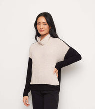 Load image into Gallery viewer, A woman modeling a colorblock turtleneck top with an oatmeal body and black sleeves, paired with black pants, against a plain white background.

