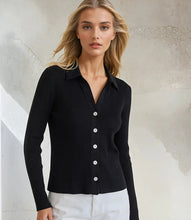 Load image into Gallery viewer, Woman wearing a black ribbed long sleeve top with buttons and white pants against a neutral background.
