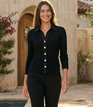 Load image into Gallery viewer, Woman wearing a black button-up shirt and black pants standing outdoors with a building and plants in the background.
