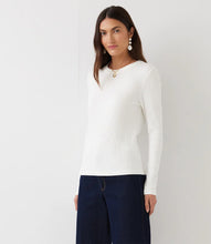 Load image into Gallery viewer, A woman modeling a white ribbed long-sleeve top paired with dark blue jeans, against a plain light gray background.
