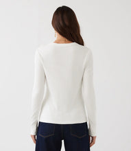 Load image into Gallery viewer, A woman viewed from the back wearing a ribbed long-sleeve knit top in off-white and dark blue jeans, against a plain light gray studio background.

