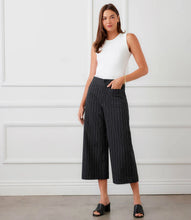 Load image into Gallery viewer, Woman wearing an off-white sleeveless tank top, black pinstripe pants and black sandals against a white wall.
