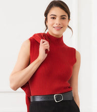Load image into Gallery viewer, Woman wearing a red sleeveless ribbed turtleneck sweater, black skirt and black belt against a white wall.
