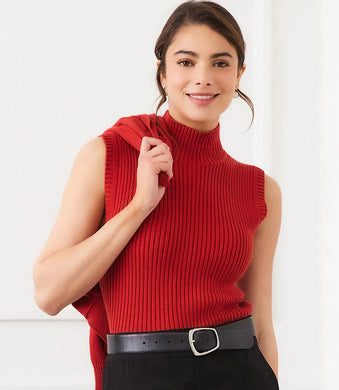 Woman wearing a red sleeveless ribbed turtleneck sweater, black skirt and black belt against a white wall.