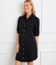 Load image into Gallery viewer, Woman wearing a black button-up shirt dress against a white wall.
