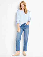 Load image into Gallery viewer, Woman wearing a light blue sweater with a ruffle along the sleeves, blue jeans and tan flats against a white background.
