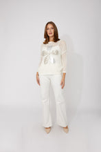 Load image into Gallery viewer, Woman wearing a white mesh top with a decorative silver sequin flower, white pants and beige heels on a plain background.
