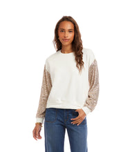 Load image into Gallery viewer, Woman wearing an off-white top with sequin sleeves and blue jeans against a white background.
