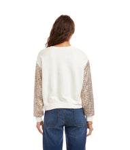 Load image into Gallery viewer, Woman wearing an off-white top with sequin sleeves and blue jeans against a white background.
