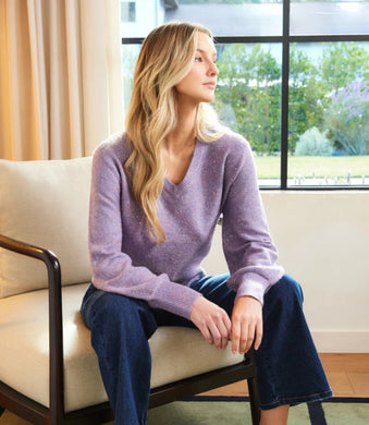 Woman sitting on a chair wearing a purple sequin sweater and blue jeans, looking out a window.