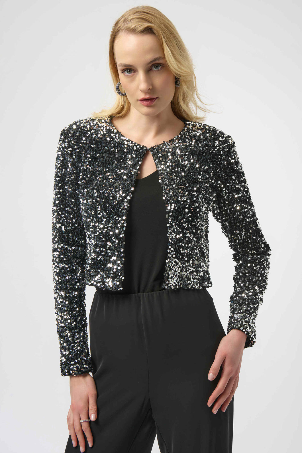 Woman wearing a black and silver sequined long sleeve jacket over a black top and black pants against a white background.