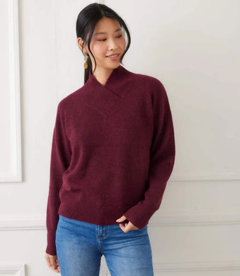 Woman wearing a burgundy sweater and blue jeans against a white wall.