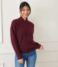 Load image into Gallery viewer, Woman wearing a burgundy sweater and blue jeans against a white wall.
