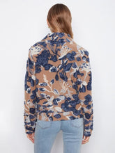 Load image into Gallery viewer, A woman modeling a long-sleeve button-up coat with a camel, navy, and white abstract floral pattern, paired with light-wash blue jeans and black ankle boots, standing against a white wall.
