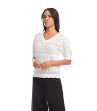 Load image into Gallery viewer, Woman wearing an off-white, short sleeve crochet top and black pants against a white background.
