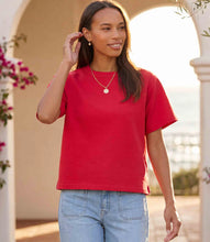 Load image into Gallery viewer, Woman wearing a red short sleeve shirt and blue jeans standing outdoors.
