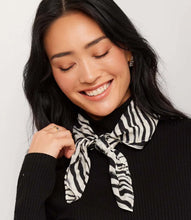 Load image into Gallery viewer, A woman with long black hair smiling and looking down, wearing a black ribbed turtleneck sweater and a black and white zebra-print neck scarf tied at the collar.
