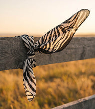 Load image into Gallery viewer, A lightweight scarf with a zebra stripe pattern tied in a knot and draped over a rustic wooden fence post in an outdoor field at sunset.
