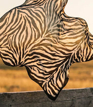 Load image into Gallery viewer, A lightweight square scarf with a zebra print pattern in black and white, draped dynamically outdoors over a rustic wooden fence with a blurred natural background.
