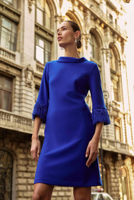 Woman wearing a blue dress with fringe cuffs in an urban setting.