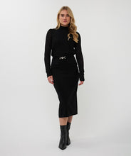 Load image into Gallery viewer, Woman wearing a black turtleneck and long black skirt with gold buckle and black boots against a white background.
