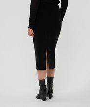 Load image into Gallery viewer, Model wearing a long black skirt with a back slit against a white background.
