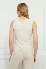 Load image into Gallery viewer, Woman wearing a vanilla-colored sleeveless top and pants against a white wall.
