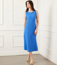 Load image into Gallery viewer, Woman wearing a blue dress standing against a white paneled wall.
