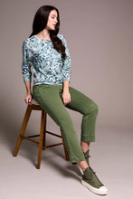 Load image into Gallery viewer, Woman sitting on a bench wearing a patterned green, blue, white sweater, green pants and green sneakers against a pale pink background.
